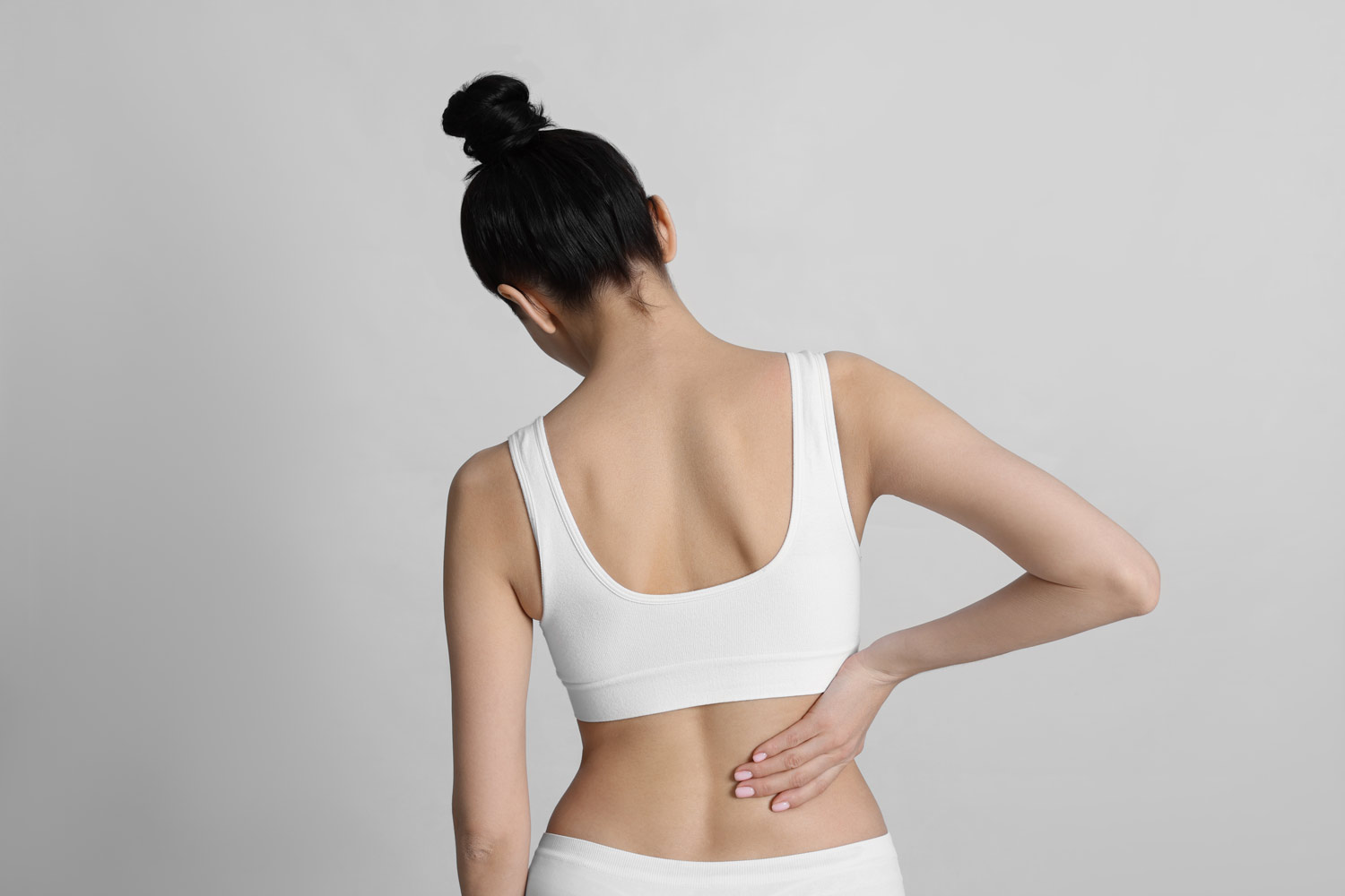 Woman with scoliosis holding her back - CorePosture Chiropractic in Newport Beach
